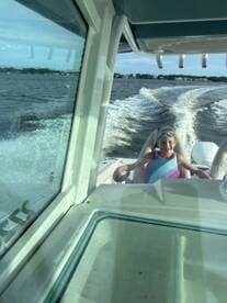 A young girl enjoys a fun day on the water, steering a boat with a big smile — perfect for family adventures and creating lasting memories.