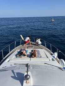 A group enjoys a relaxing day on a yacht, sunbathing on the deck while surrounded by the serene blue waters — perfect for a summer getaway.