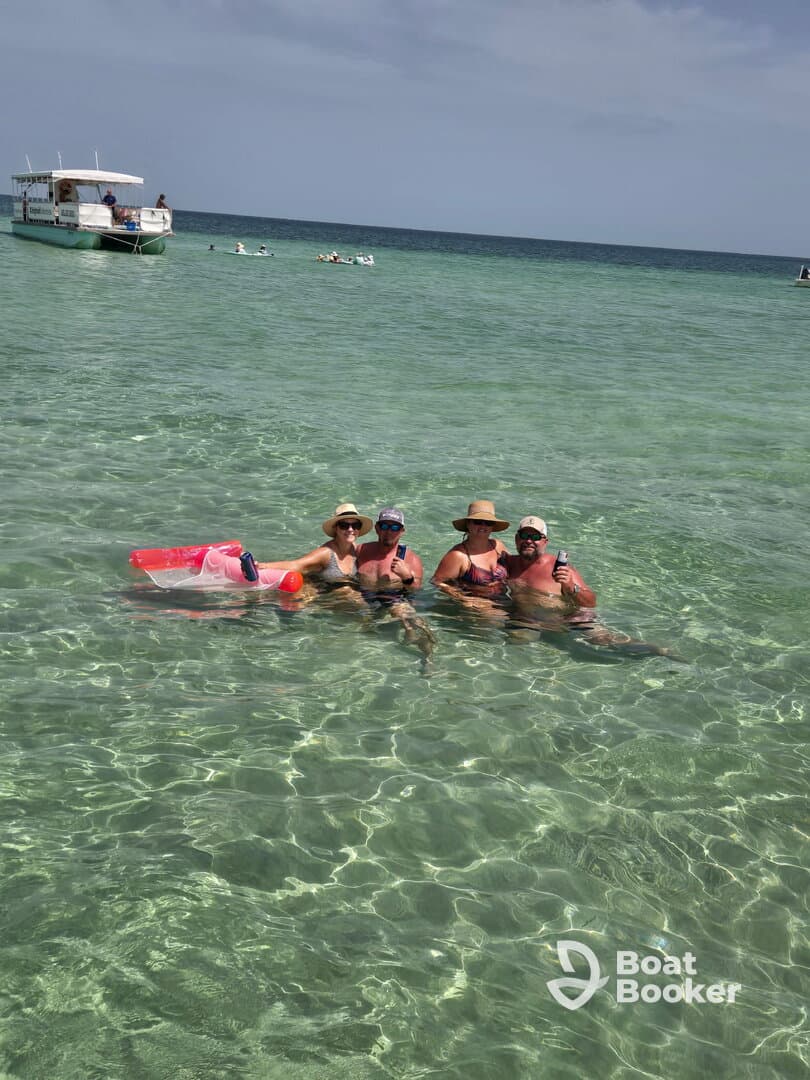 A cheerful group enjoys a refreshing swim in crystal-clear waters, sipping cocktails and soaking up the sun — a perfect beach day experience.