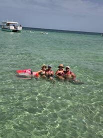 A cheerful group enjoys a refreshing swim in crystal-clear waters, sipping cocktails and soaking up the sun — a perfect beach day experience.