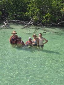 A cheerful group enjoys a refreshing swim in clear waters surrounded by mangroves, capturing the essence of a fun day on the water.