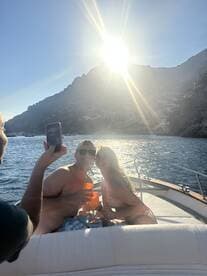 A happy couple enjoys cocktails on a boat under the bright sun, capturing a perfect moment of celebration against a stunning coastal backdrop.
