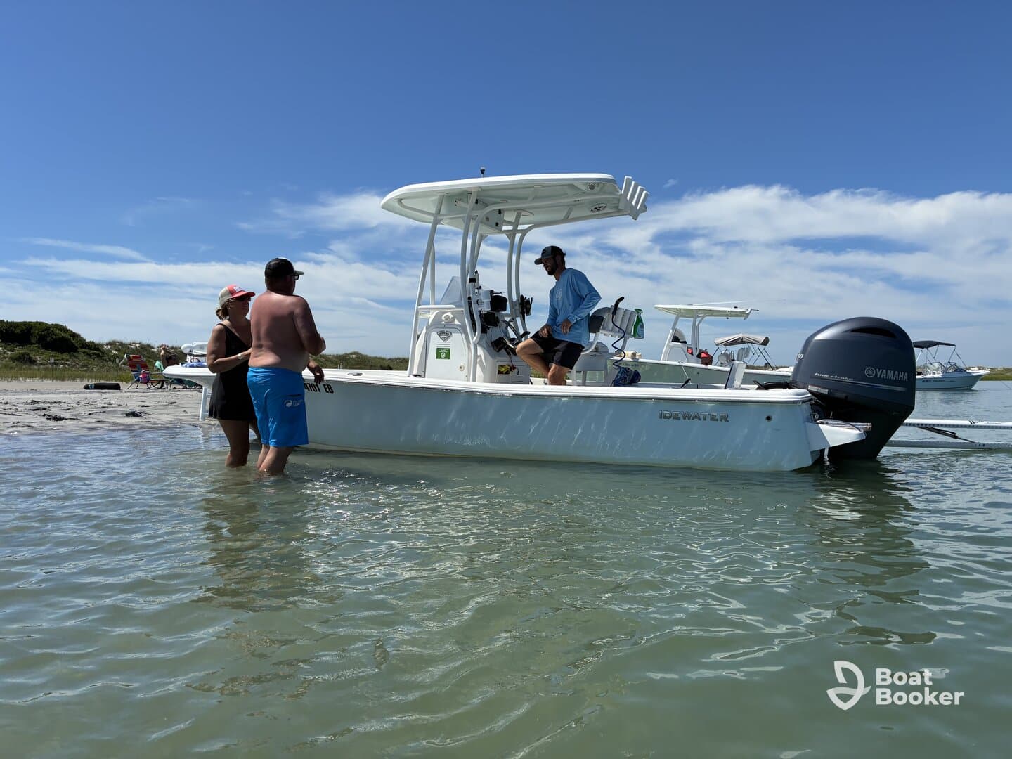 A group enjoys a sunny day at the beach, interacting around their boat in shallow water — perfect for a fun-filled day on the water.
