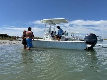 A group enjoys a sunny day at the beach, interacting around their boat in shallow water — perfect for a fun-filled day on the water.