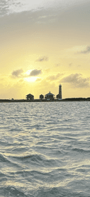 A stunning sunset view featuring a lighthouse and coastal buildings, creating a picturesque backdrop over the water — perfect for capturing the beauty of maritime landscapes.