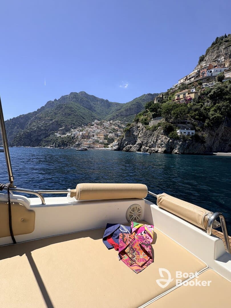 A cozy seating area on a boat, featuring colorful towels laid out, with a stunning coastal view in the background — perfect for relaxing on the water.