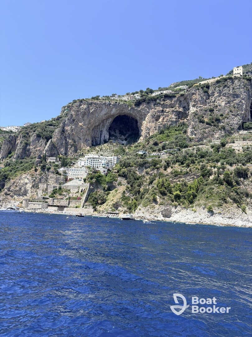 A stunning view of a coastal cliff with a natural cave and picturesque buildings, showcasing the beauty of the landscape along the water's edge.