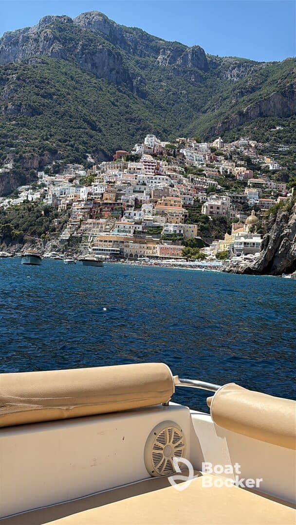 A stunning view of the colorful coastal town along the Amalfi Coast, captured from a boat, showcasing the beautiful architecture and lush mountains in the background.
