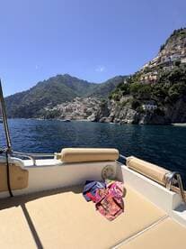A cozy seating area on a boat, featuring colorful towels laid out, with a stunning coastal view in the background — perfect for relaxing on the water.