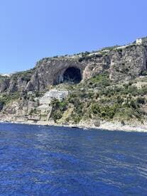 A stunning view of a coastal cliff with a natural cave and picturesque buildings, showcasing the beauty of the landscape along the water's edge.