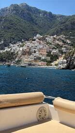 A stunning view of the colorful coastal town along the Amalfi Coast, captured from a boat, showcasing the beautiful architecture and lush mountains in the background.
