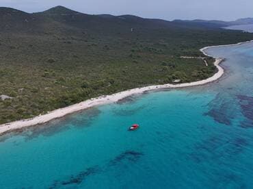 A stunning aerial view of a secluded beach with turquoise waters and a vibrant red boat anchored nearby, perfect for showcasing the beauty of island destinations.