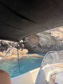 A view from inside a boat's cabin, showcasing the helm and shaded area while navigating near rocky cliffs and clear blue waters.