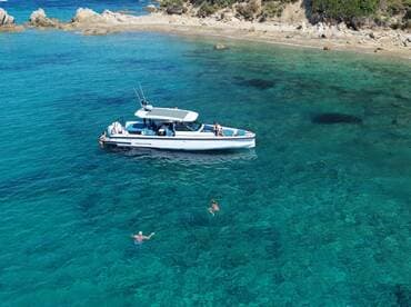 A group enjoys a sunny day on the water, with some swimming and others relaxing on the boat, showcasing the perfect summer getaway.