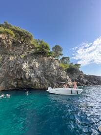 A group enjoys a refreshing swim in crystal-clear waters near a rocky coastline, with a boat anchored nearby — perfect for snorkeling adventures and coastal exploration.