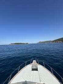 A stunning view from the front of a yacht cruising through clear blue waters, with a picturesque island in the distance — perfect for exploring coastal destinations.