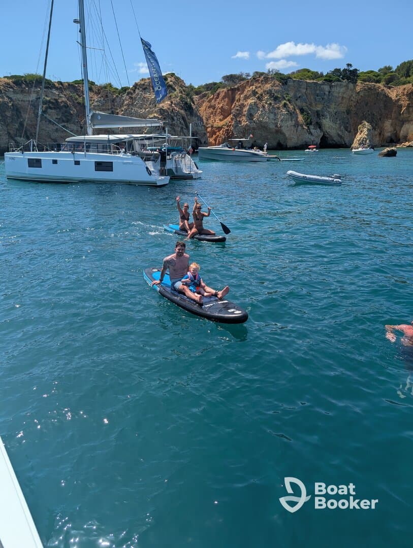 A joyful family enjoys paddleboarding in the ocean, showcasing a fun day on the water with stunning cliffs in the background.