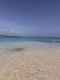 A serene view of a clear turquoise beach with gentle waves, perfect for relaxation and enjoying the beauty of nature.