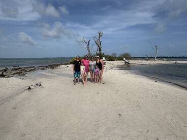 A joyful family poses together on a sandy beach, capturing a memorable moment during their sandbar adventure — perfect for family outings and beach fun.
