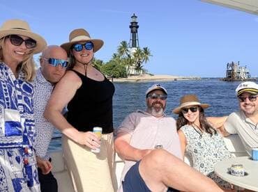 A cheerful group of friends enjoys a day on the water, posing with a scenic lighthouse in the background — perfect for memorable boating adventures.