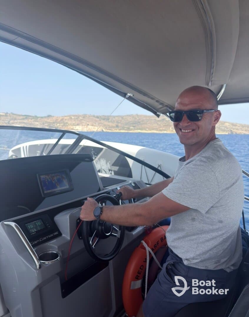 A man confidently navigates the helm of a modern boat, showcasing the sleek interior and advanced controls — perfect for a day of adventure on the water.