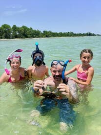 A family enjoys a fun snorkeling adventure, showcasing a crab caught in shallow waters — a perfect moment for wildlife interaction and family bonding.