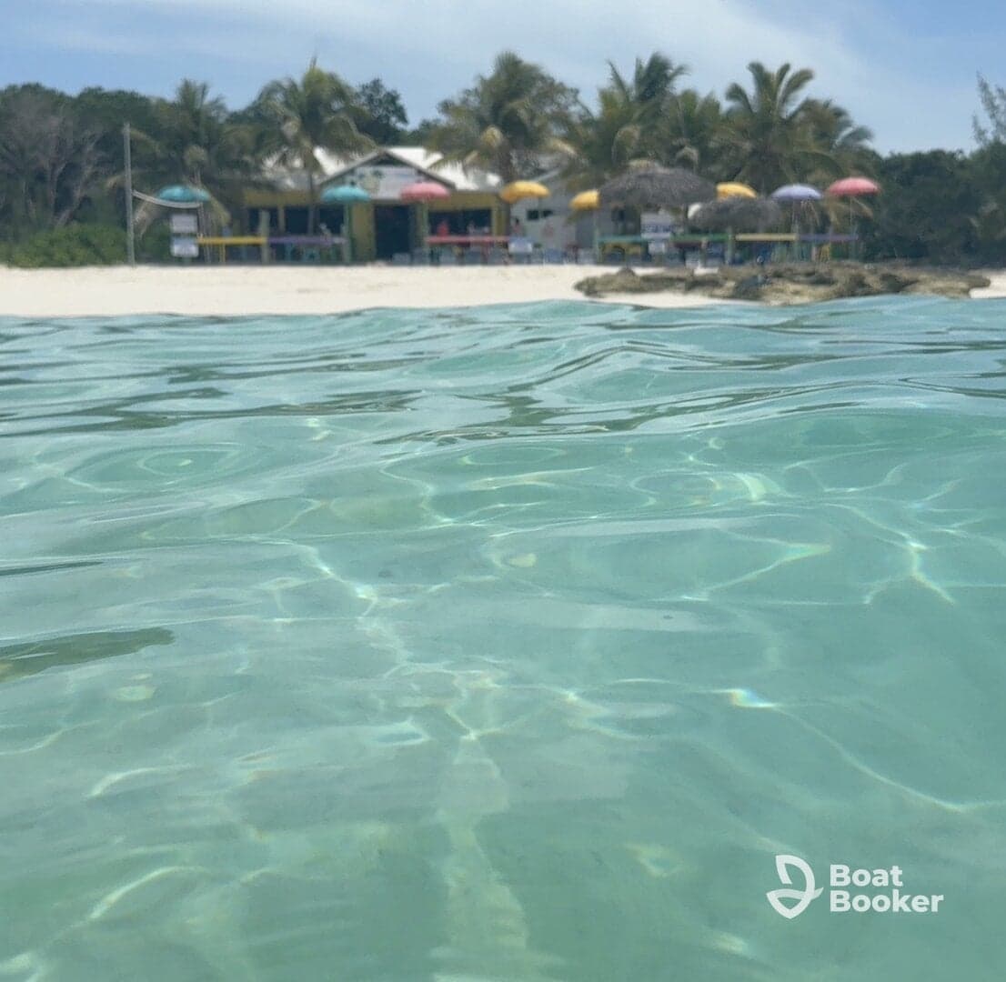 A serene view of a beachside establishment with colorful umbrellas, captured from the clear waters — perfect for a relaxing day by the shore.