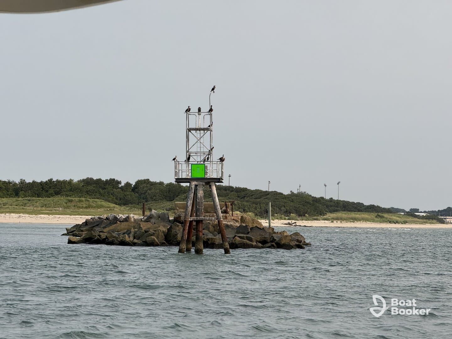 An unclear view of a lighthouse structure on a rocky outcrop, surrounded by water and greenery in the background.