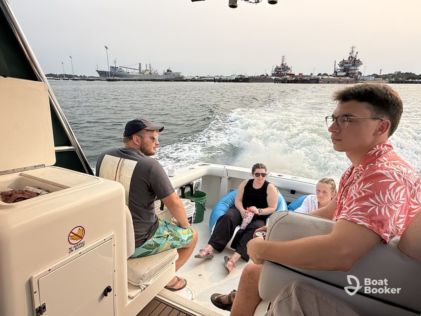 A group of friends enjoys a day on the water, relaxing on a boat with scenic views of the harbor in the background.