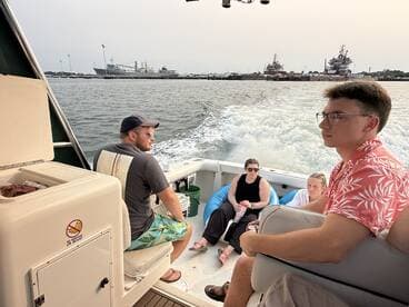 A group of friends enjoys a day on the water, relaxing on a boat with scenic views of the harbor in the background.
