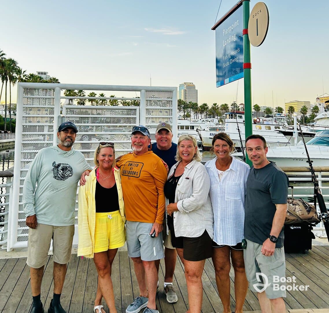 A cheerful group of friends poses together at the marina, ready for a day of boating adventures. The scenic backdrop features a variety of boats and palm trees, perfect for a fun outing.