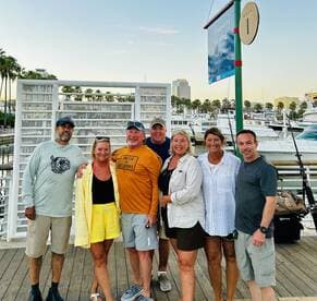 A cheerful group of friends poses together at the marina, ready for a day of boating adventures. The scenic backdrop features a variety of boats and palm trees, perfect for a fun outing.