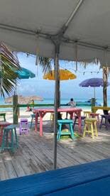 A vibrant beachside scene featuring colorful tables and umbrellas, with a person seated, creating a relaxed atmosphere perfect for enjoying the ocean view.