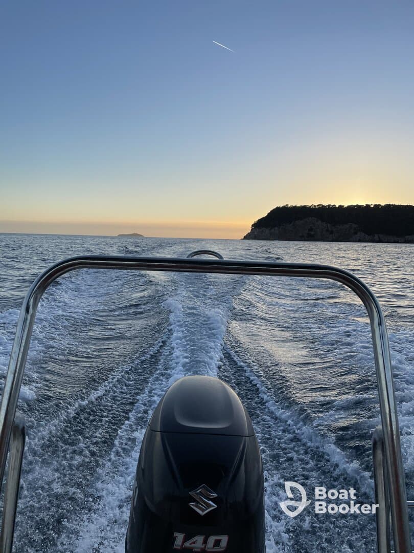 A striking view from the back of a speedboat cruising through calm waters at sunset, showcasing the engine and wake trailing behind.