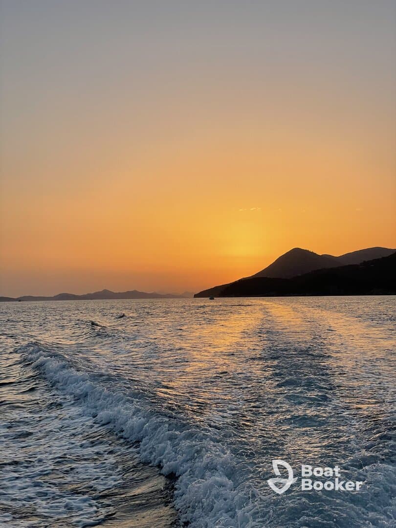 A stunning sunset over the coastline, with gentle waves reflecting the warm hues of the evening sky — a perfect backdrop for a serene boating experience.