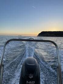 A striking view from the back of a speedboat cruising through calm waters at sunset, showcasing the engine and wake trailing behind.