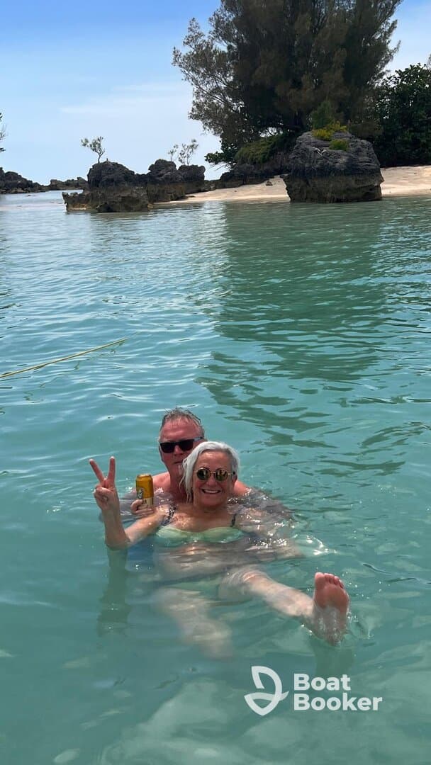 A joyful couple enjoys a refreshing swim in crystal-clear waters, celebrating their day at the beach with drinks in hand.