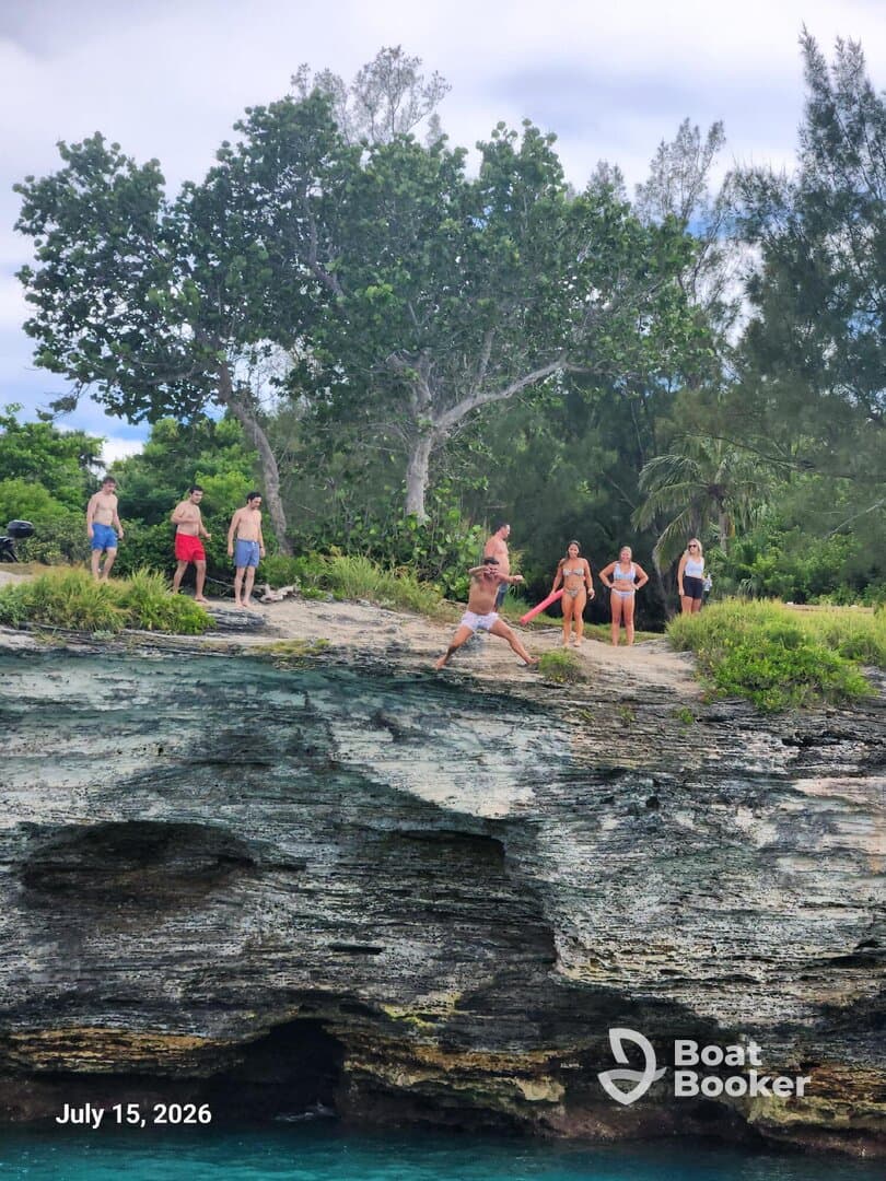 A lively group enjoys a day of adventure by the water, with some preparing to jump off a cliff into the turquoise sea — perfect for thrill-seekers and outdoor fun.