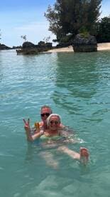 A joyful couple enjoys a refreshing swim in crystal-clear waters, celebrating their day at the beach with drinks in hand.