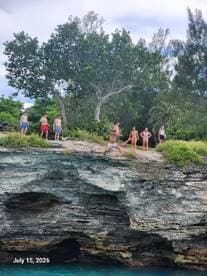 A lively group enjoys a day of adventure by the water, with some preparing to jump off a cliff into the turquoise sea — perfect for thrill-seekers and outdoor fun.