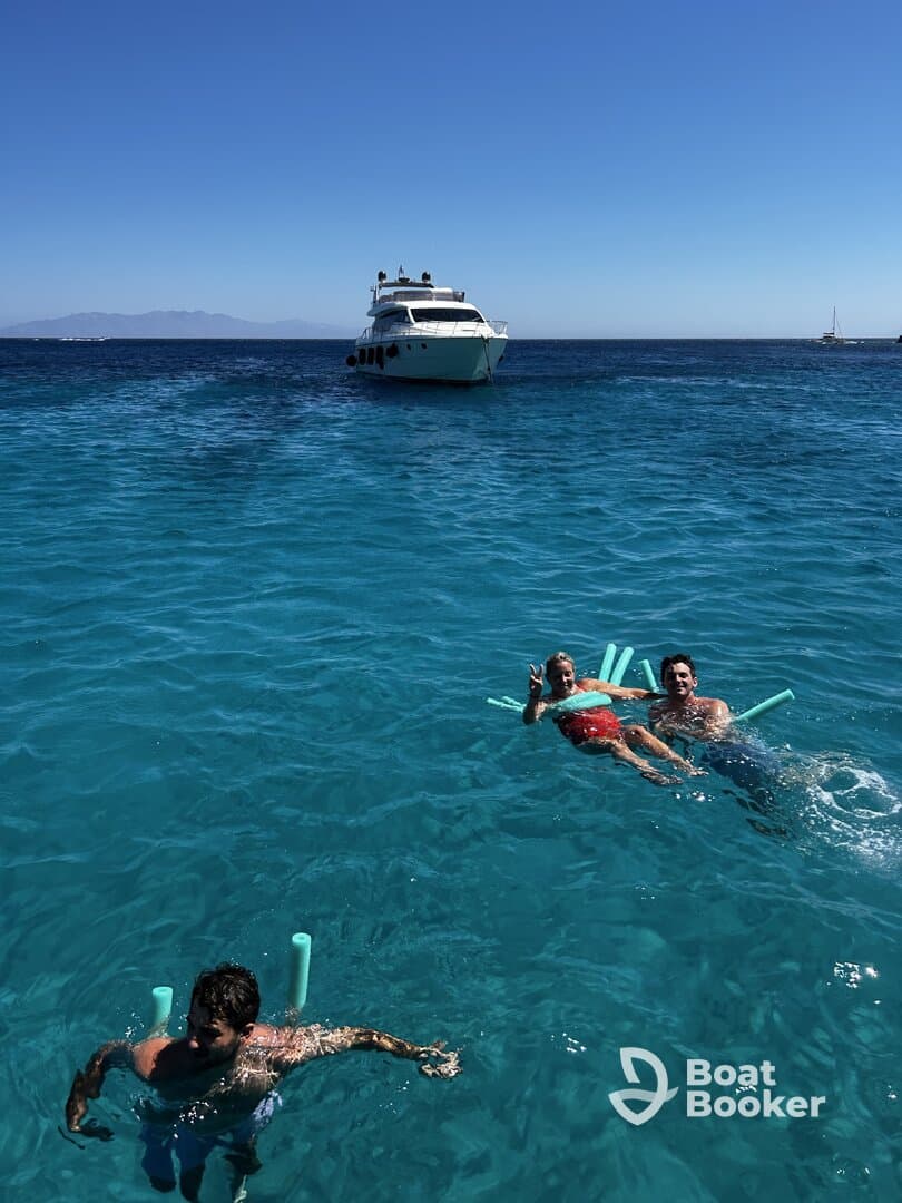 A lively group enjoys a sunny day swimming in crystal-clear waters, with a yacht anchored nearby — perfect for a fun day on the water.
