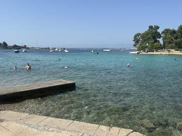 A vibrant scene of people enjoying a sunny day swimming in clear turquoise waters, with boats anchored nearby — perfect for a relaxing beach getaway.