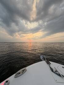 A serene sunset view from the bow of a boat, showcasing the tranquil waters and dramatic sky — perfect for romantic evening cruises.