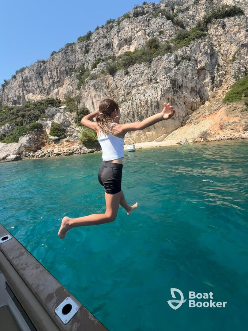 A child joyfully leaps off the side of a boat into the crystal-clear waters, capturing the essence of summer fun and adventure on the water.