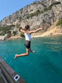 A child joyfully leaps off the side of a boat into the crystal-clear waters, capturing the essence of summer fun and adventure on the water.