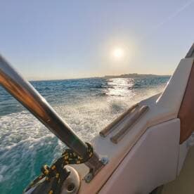 A stunning view from the side of a boat cruising through sparkling waters, with the sun setting on the horizon — perfect for showcasing the beauty of a day on the water.
