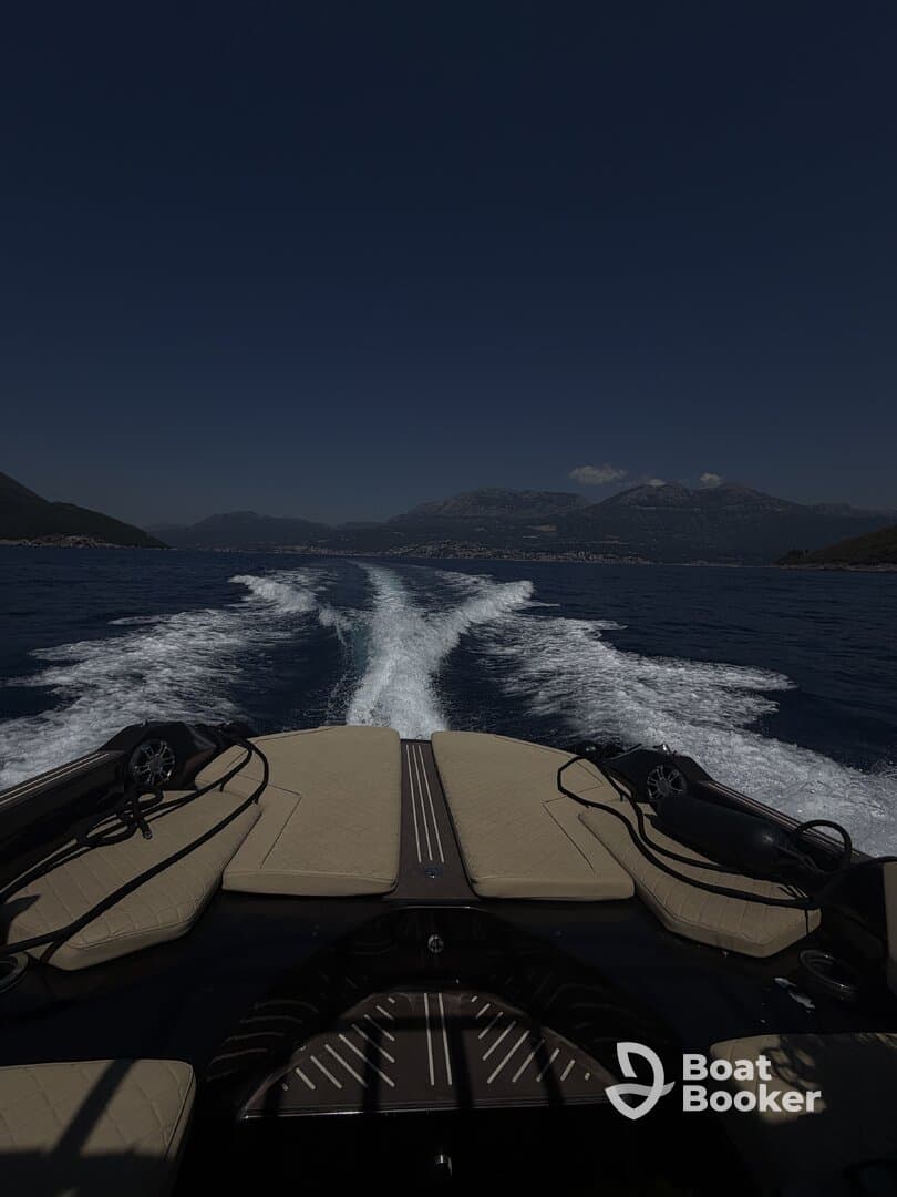 A sleek view from the back of a boat cruising through calm waters, showcasing the vessel's design and the scenic mountainous backdrop.
