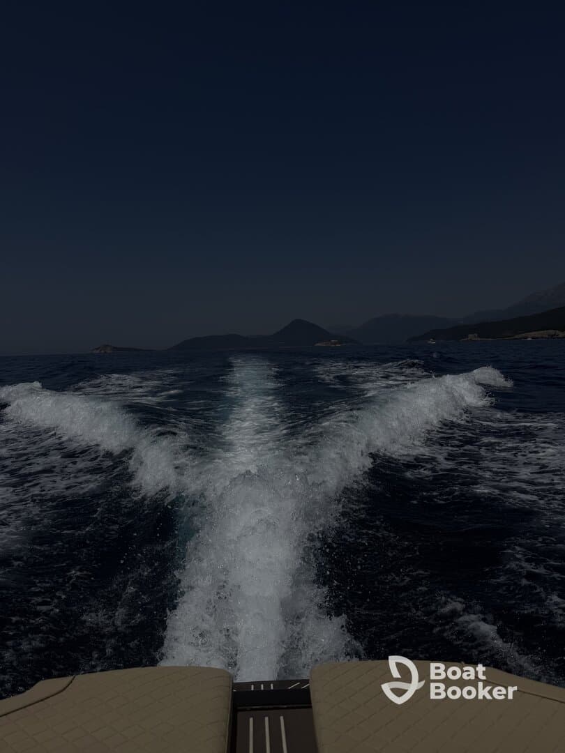 A stunning view from the back of a boat, showcasing the wake as it cuts through the water, with mountains in the background — perfect for adventure seekers exploring coastal waters.