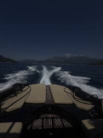 A sleek view from the back of a boat cruising through calm waters, showcasing the vessel's design and the scenic mountainous backdrop.