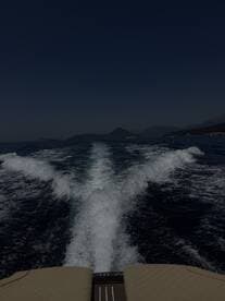 A stunning view from the back of a boat, showcasing the wake as it cuts through the water, with mountains in the background — perfect for adventure seekers exploring coastal waters.